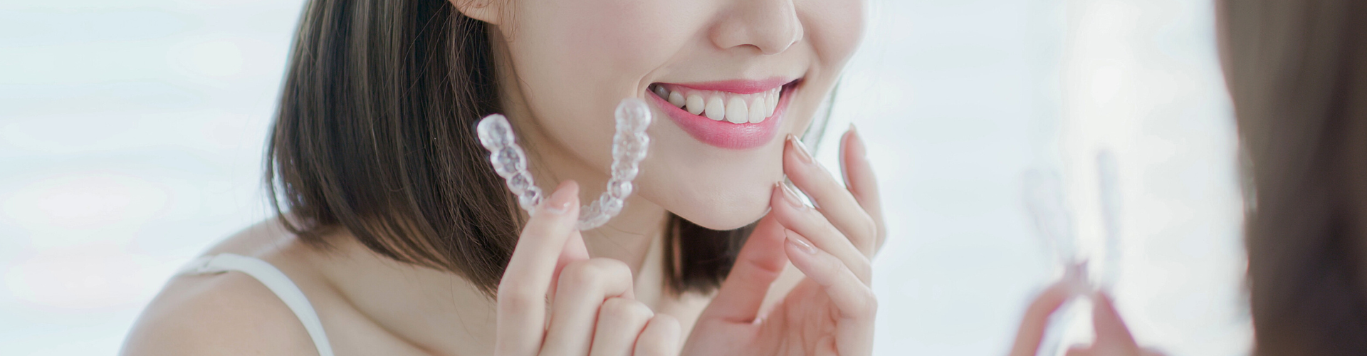Woman holding clear aligner beside her smile.